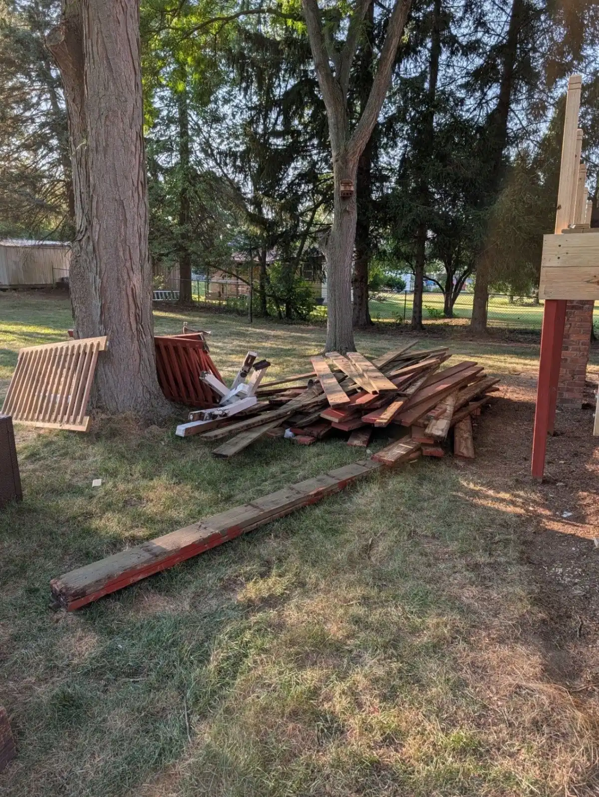 Pile of fence boards and lumber stacked in a yard beside trees