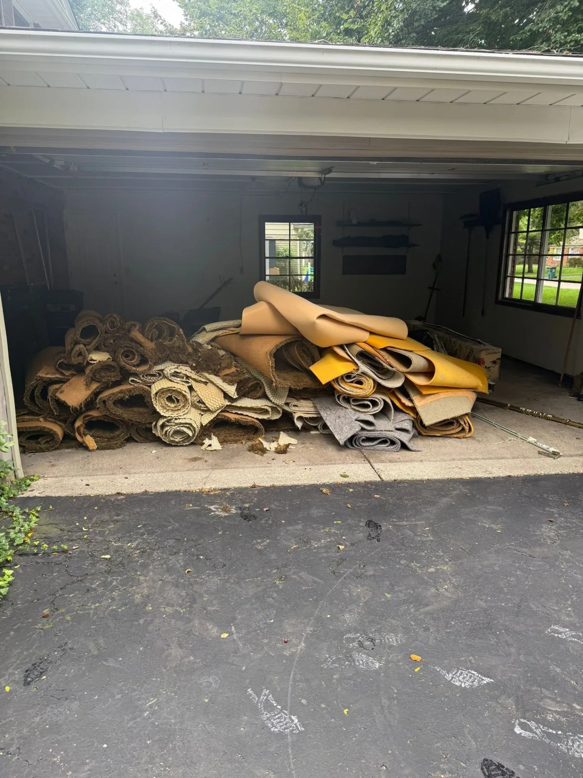 Open garage with rolled carpet, carpet padding and underlayment stacked at the doorway