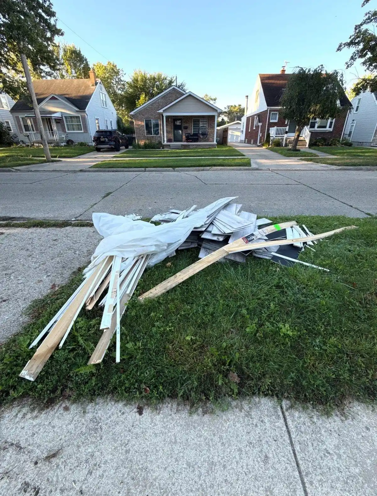 Pile of vinyl siding scraps, trim and bagged debris gathered at a curb