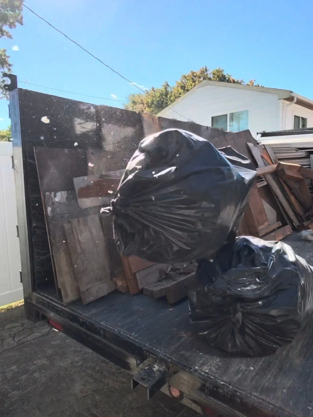 Black double-axle dump trailer loaded with bagged construction debris and stacked wood panels on a residential driveway in Royal Oak Michigan