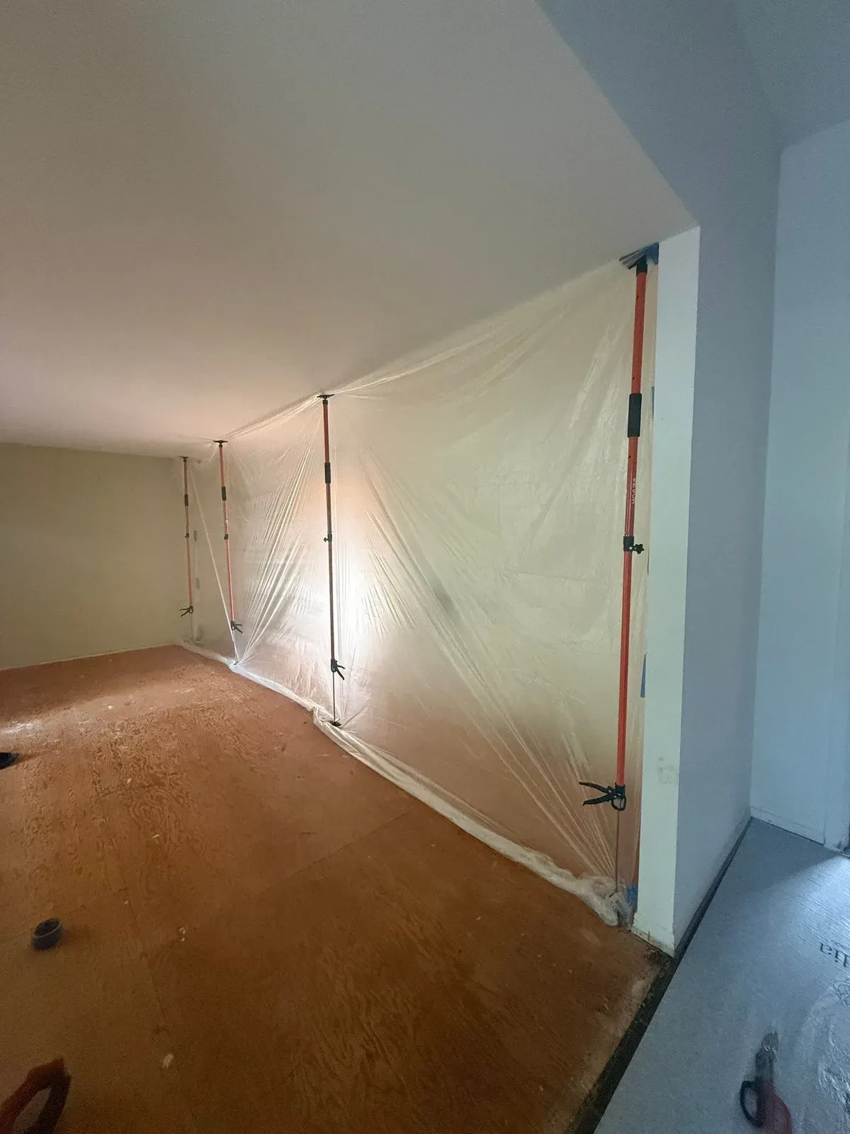 Clear plastic containment wall held by vertical spring poles across the home before kitchen demolition