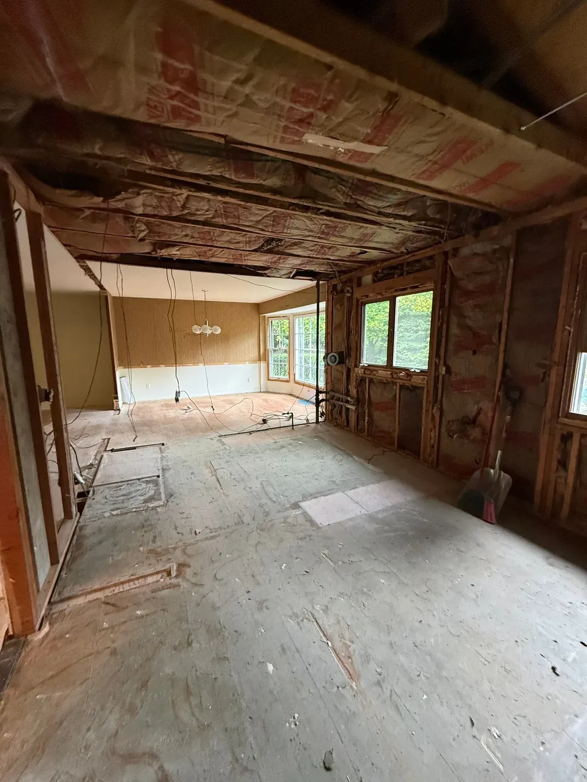 Opened wall between rooms with exposed framing, ceiling insulation and stripped plywood subfloor