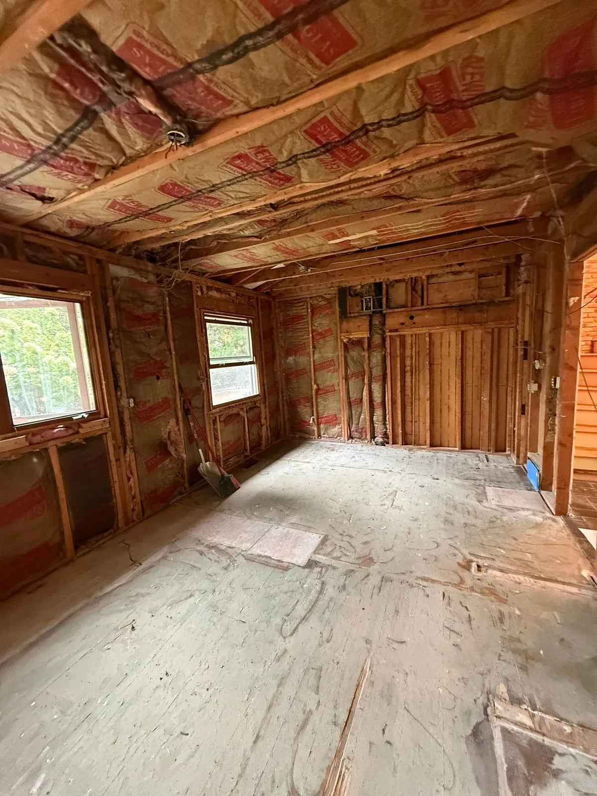 Stripped room with exposed wall studs, ceiling joists, insulation and a plywood subfloor after kitchen demolition