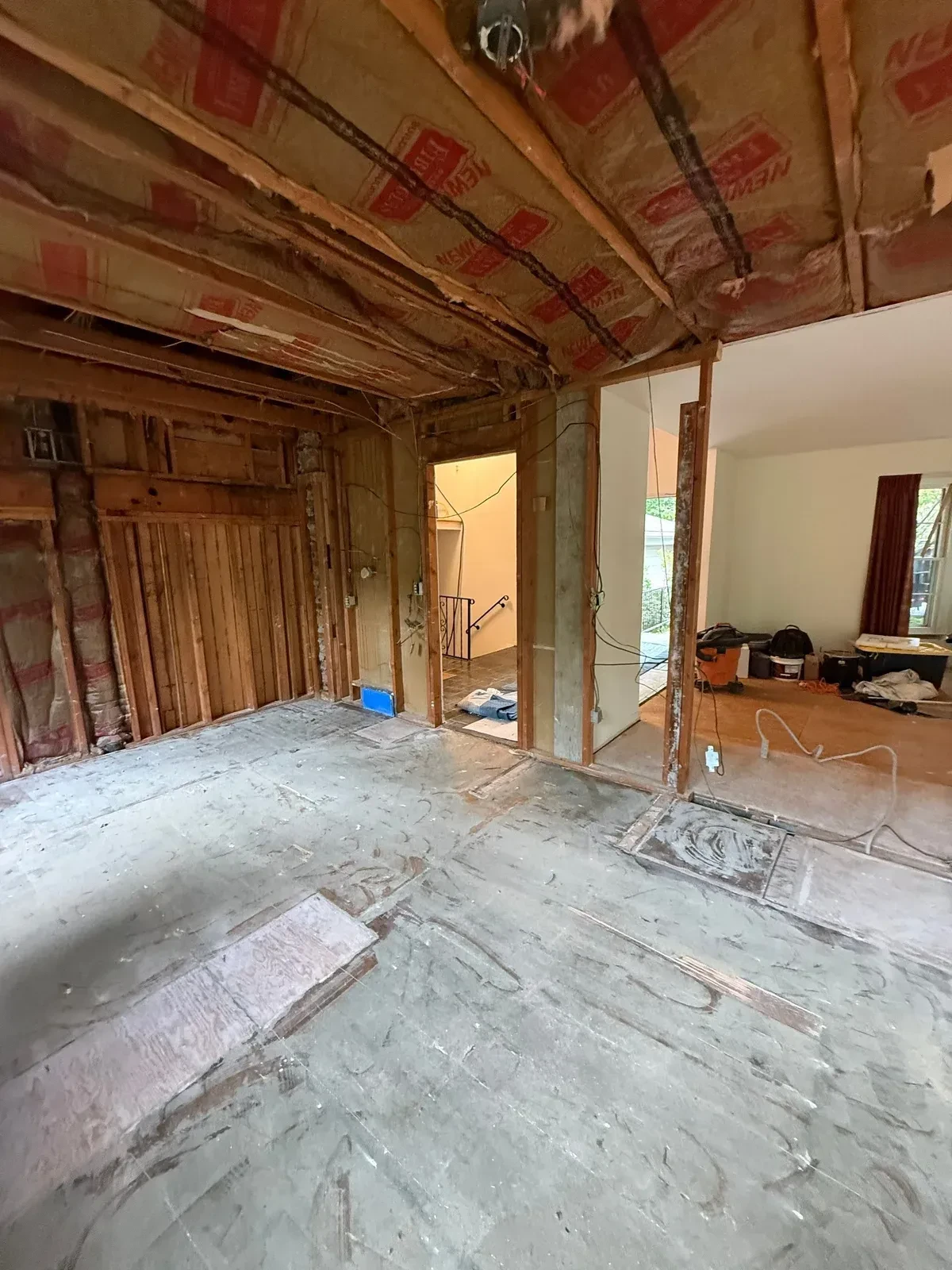 Completed wall opening to the next room with exposed framing, ceiling insulation and stripped plywood subfloor
