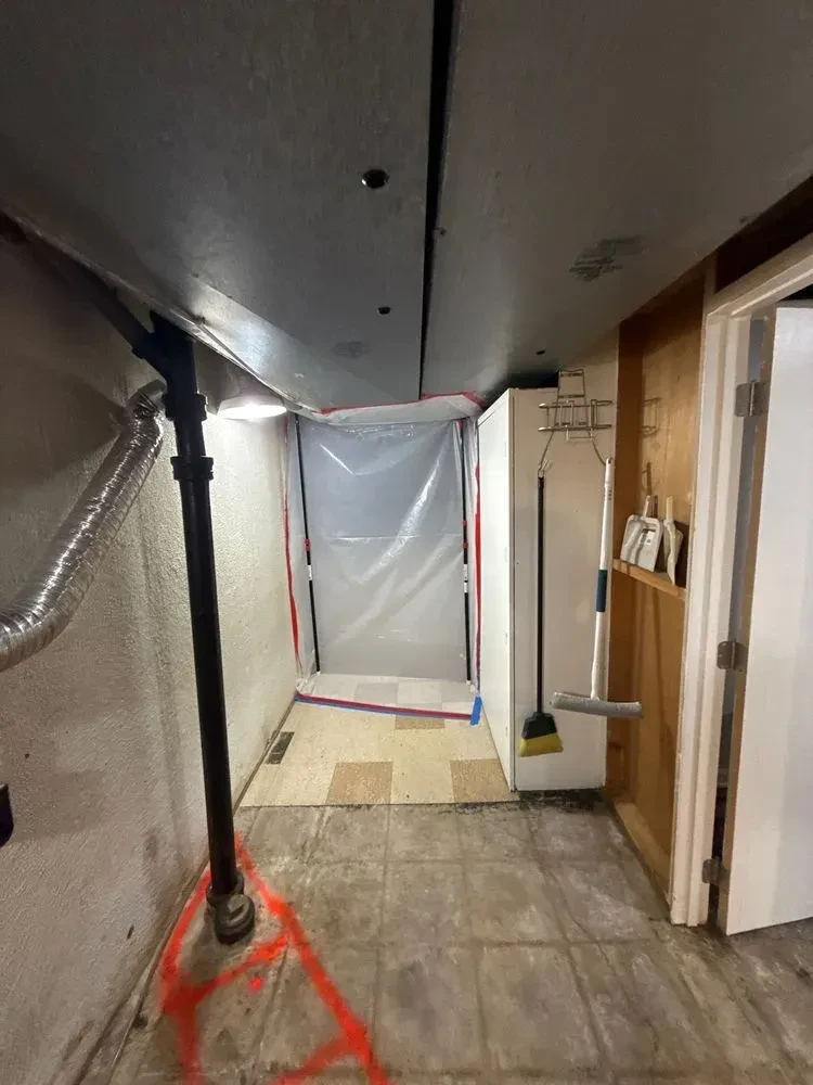 Basement hallway with a clear plastic zipper containment doorway, protective plastic and orange floor markings