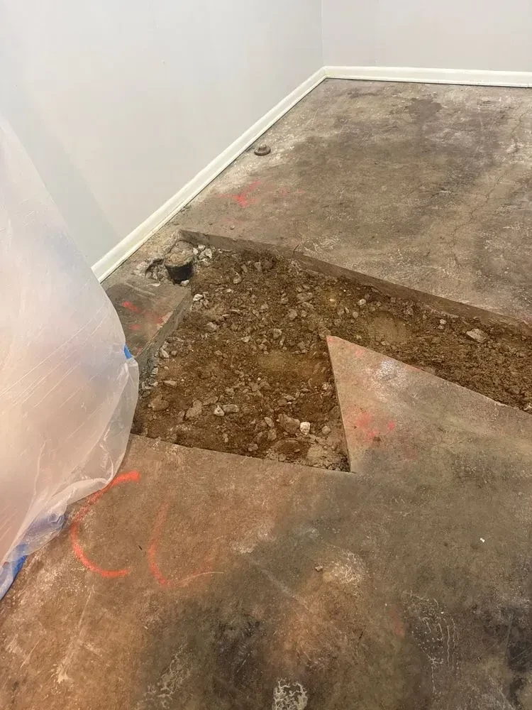 Rectangular section of basement concrete broken out to expose dirt and a floor drain
