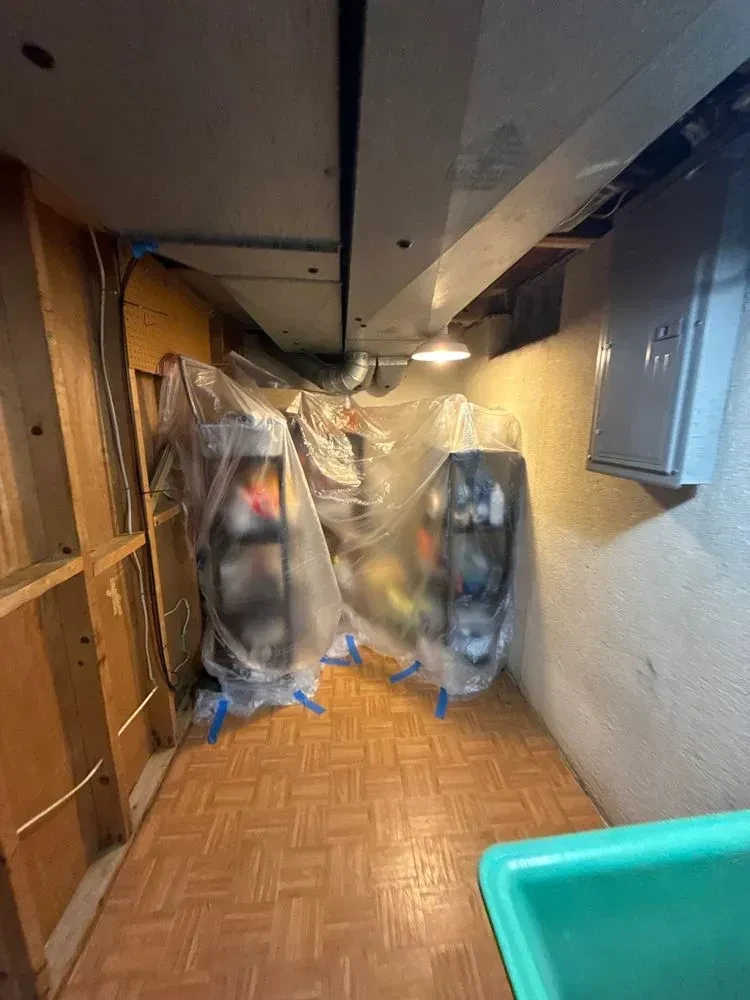 Basement work area with plastic-covered equipment and a blue tote along a finished floor