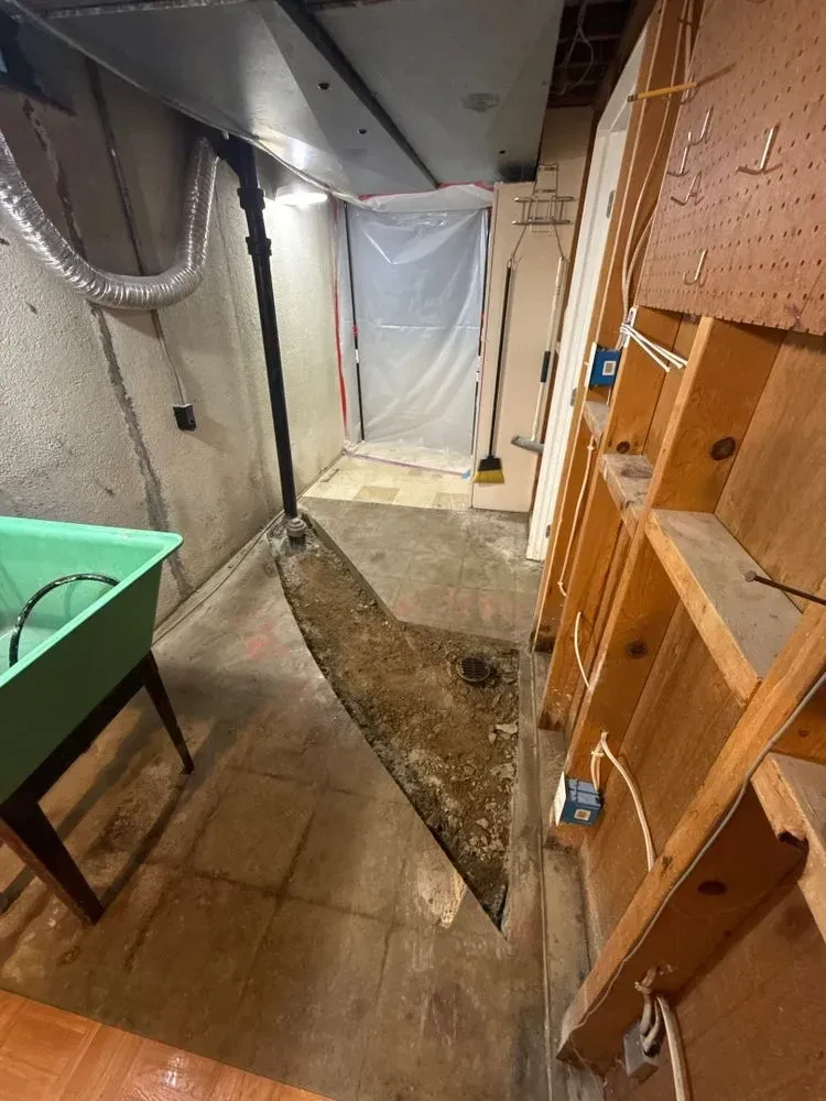 Basement concrete access trench extending across the floor with demolition equipment and a worker nearby