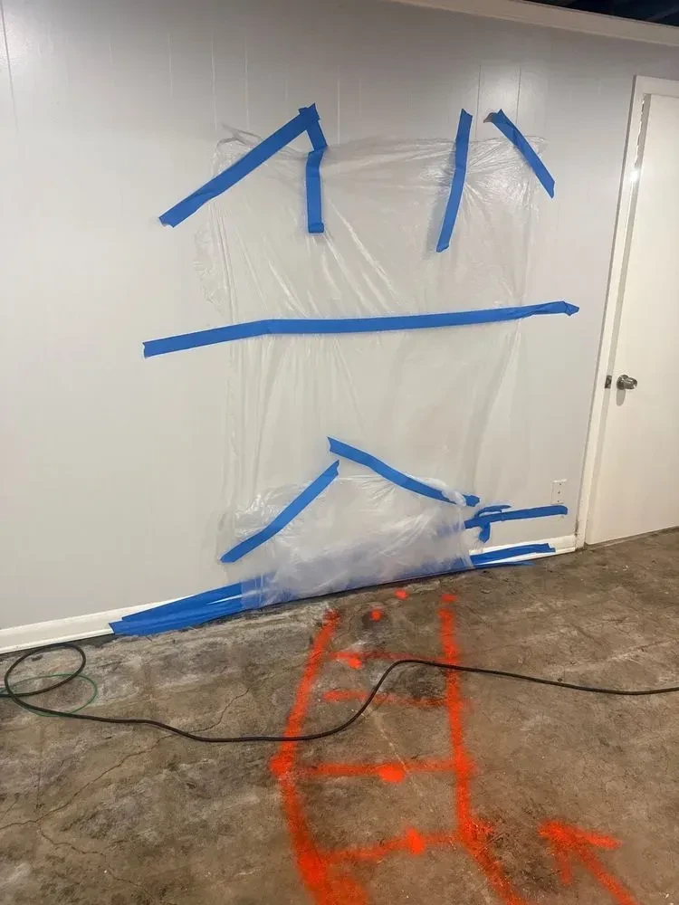 Clear plastic taped over a basement wall and lower doorway above orange floor markings