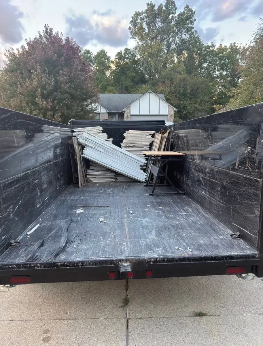 Dump trailer loaded with white ceiling panels, vinyl fence material and the wooden-top folding desk