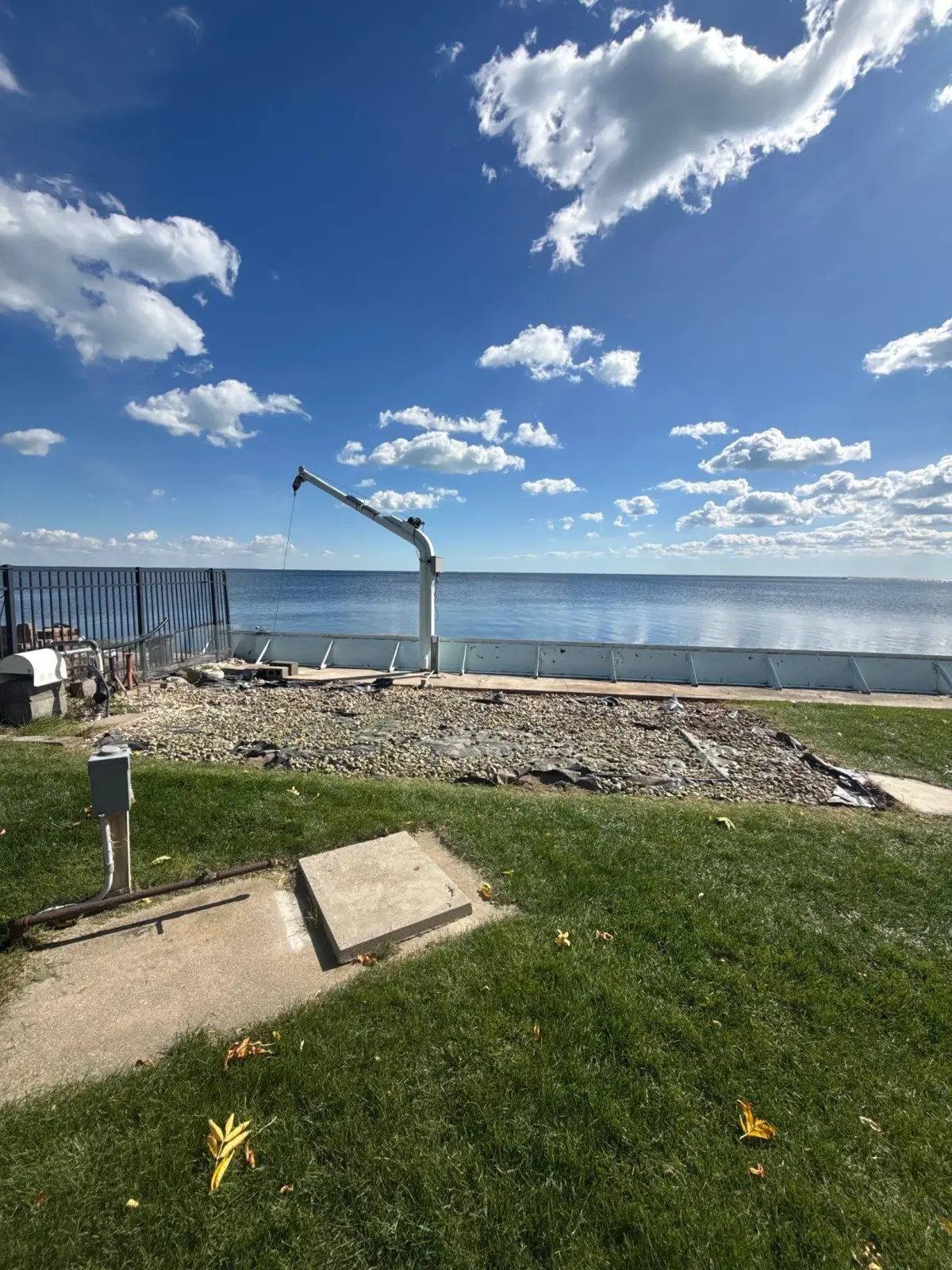 Second angle of the cleared waterfront deck area showing gravel, rock, landscape fabric, the boat hoist and the seawall