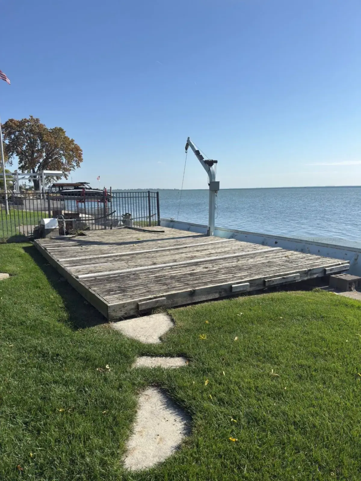 Intact wood deck at the Harrison Township waterfront before removal, with the boat hoist, seawall, lawn and concrete walkway visible