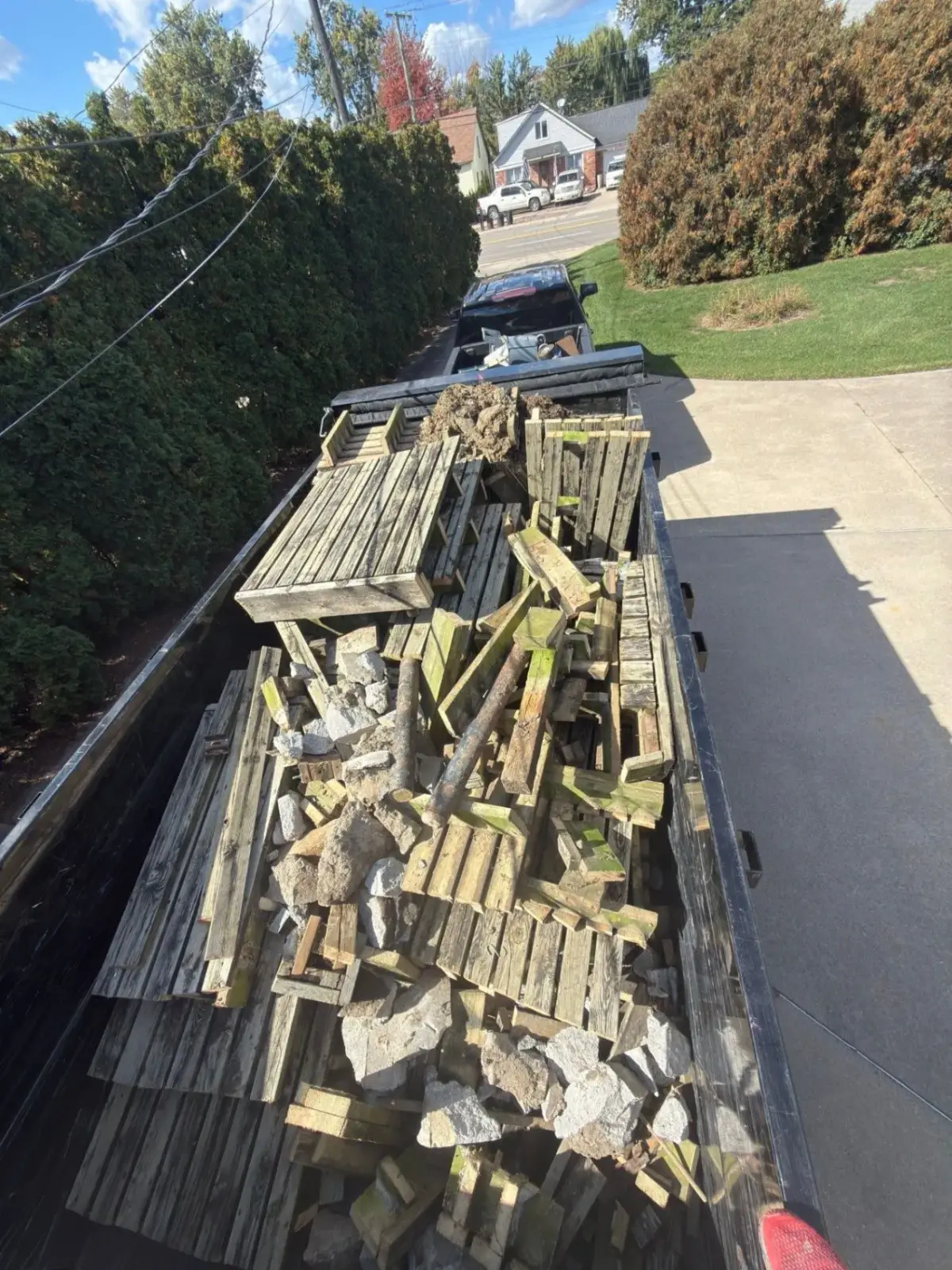Rubber-wheeled dump trailer loaded with demoed deck boards, framing and broken-out concrete, ready for haul-away