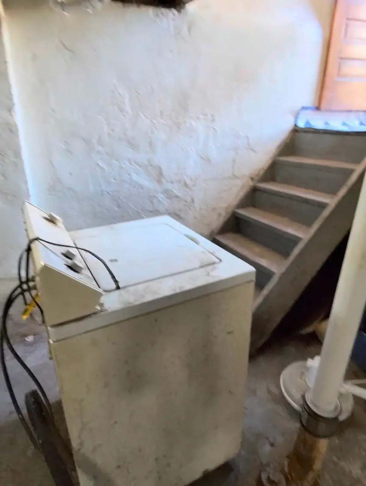 Washing machine sitting beside basement stairs before removal in St. Clair Shores