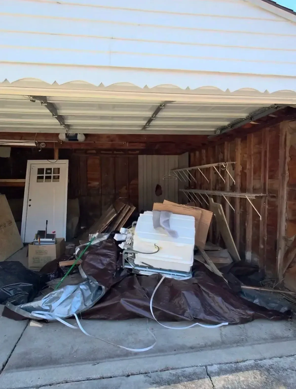 Cluttered St. Clair Shores garage interior before cleanout, with a sofa, dresser, white appliance and loose materials on the floor