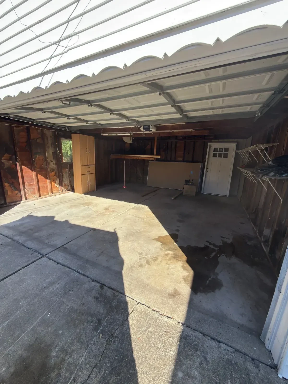 Cleared and swept garage viewed from the driveway through the open door, with a panel and 2x4s still inside