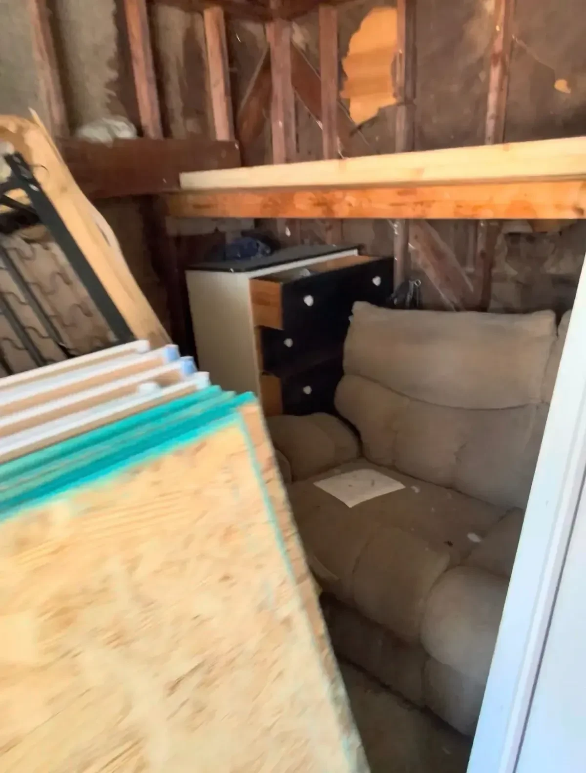 Garage interior with a sofa, dresser, wood panel and other stored items before cleanout