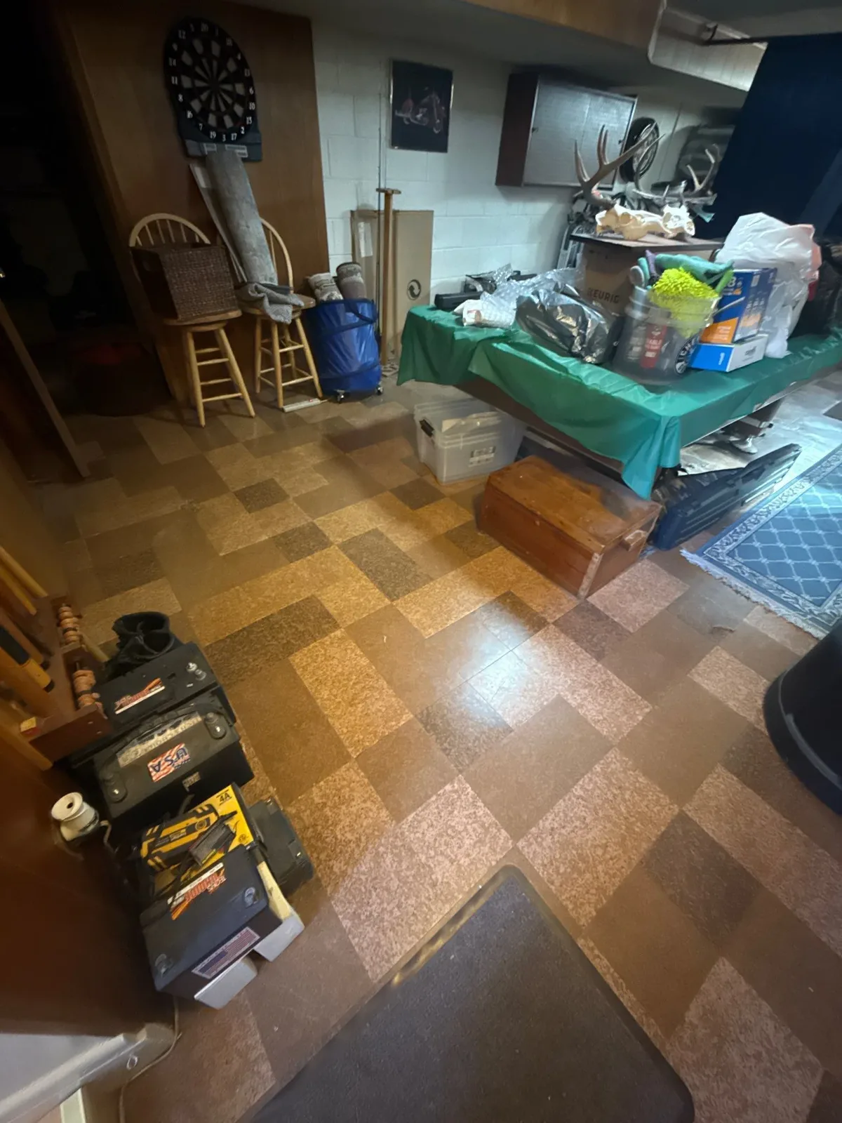 St. Clair Shores basement after junk removal, with the Total Gym and fitness exercise bike gone while chairs, tables, boxes, shelving and the green-covered table remain in place