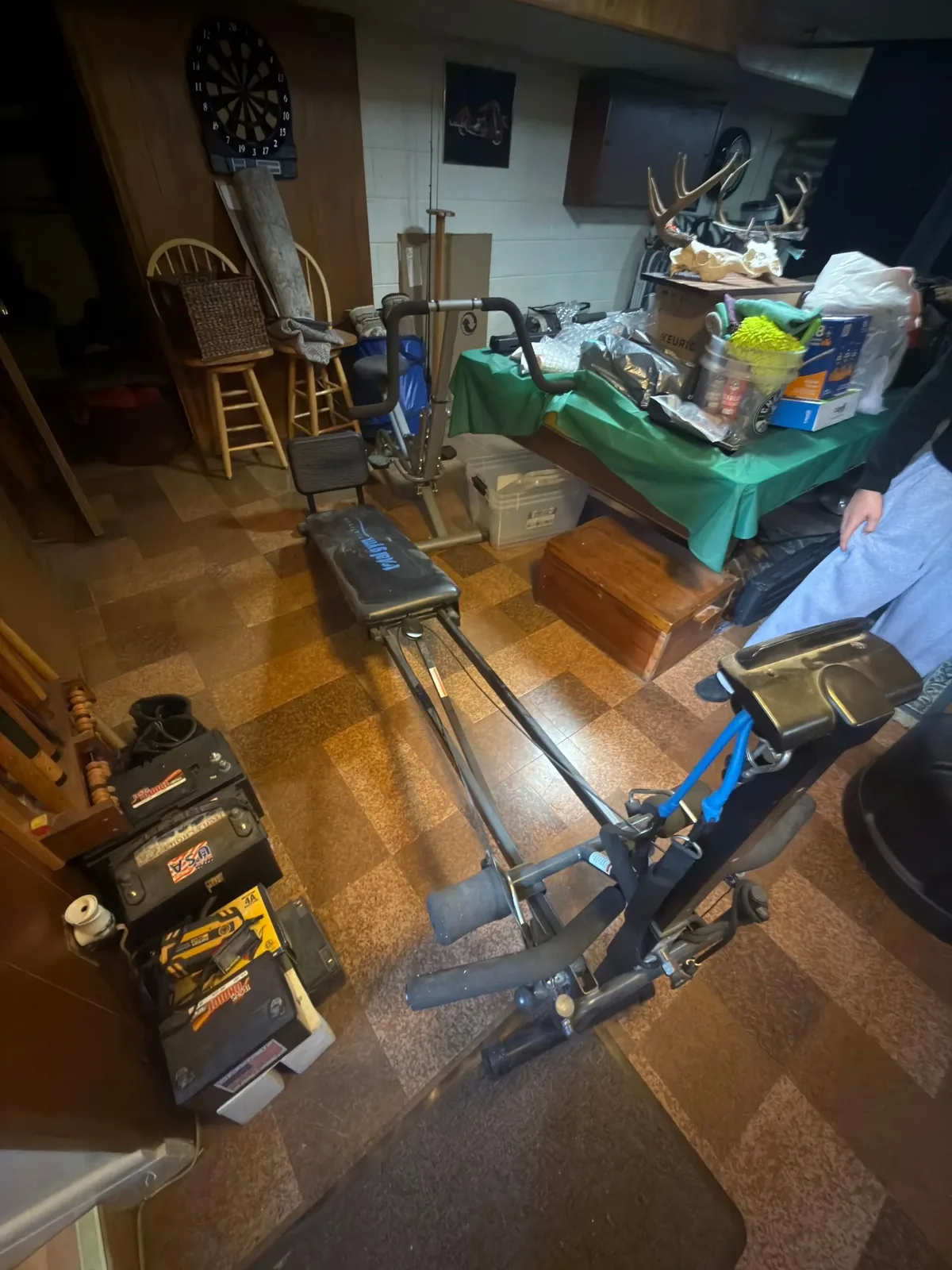 St. Clair Shores basement before junk removal, with a Total Gym and fitness exercise bike on the tiled floor and other stored household contents visible