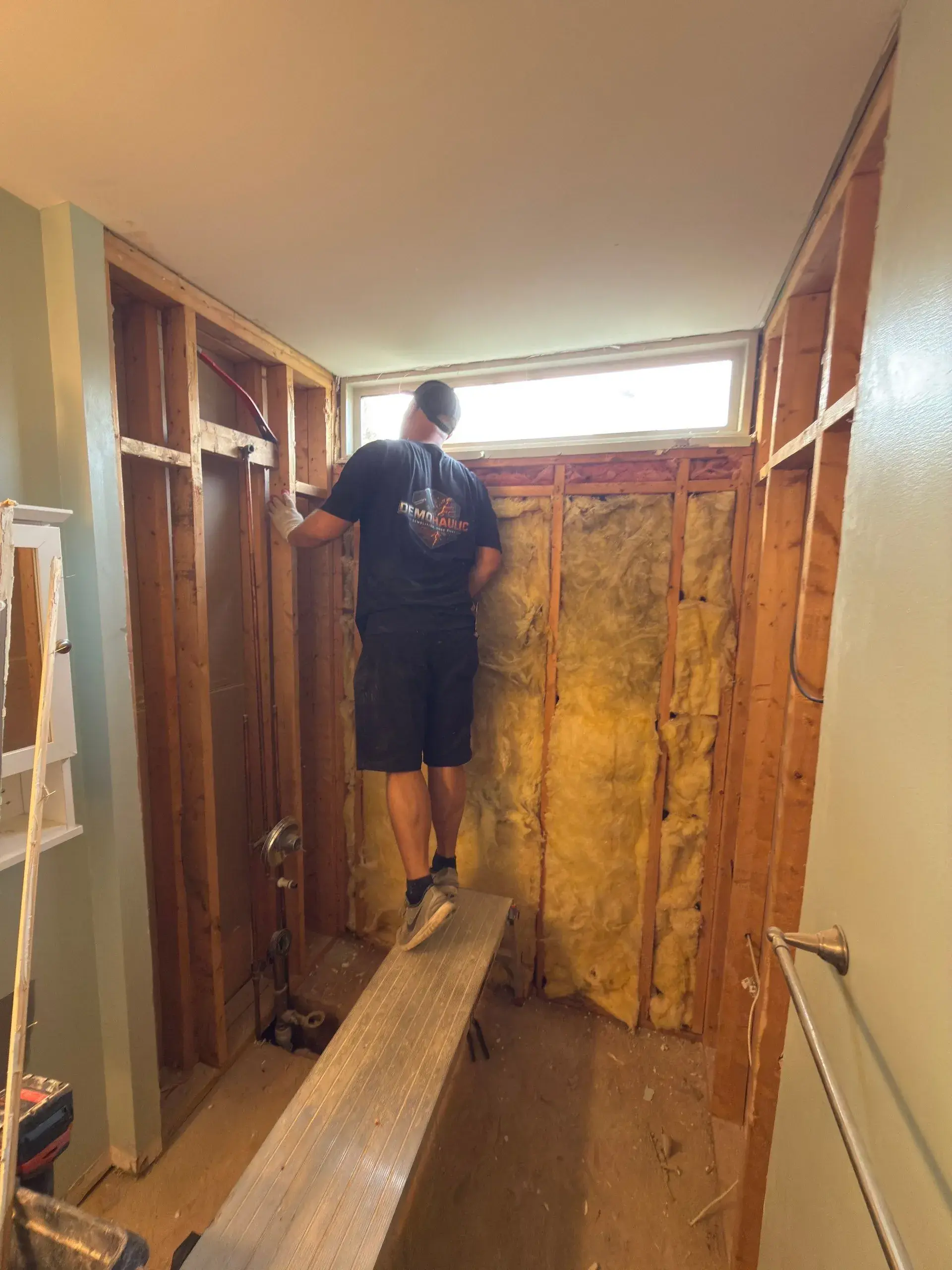 Worker in a bathroom with wall finishes removed and framing exposed around the shower area
