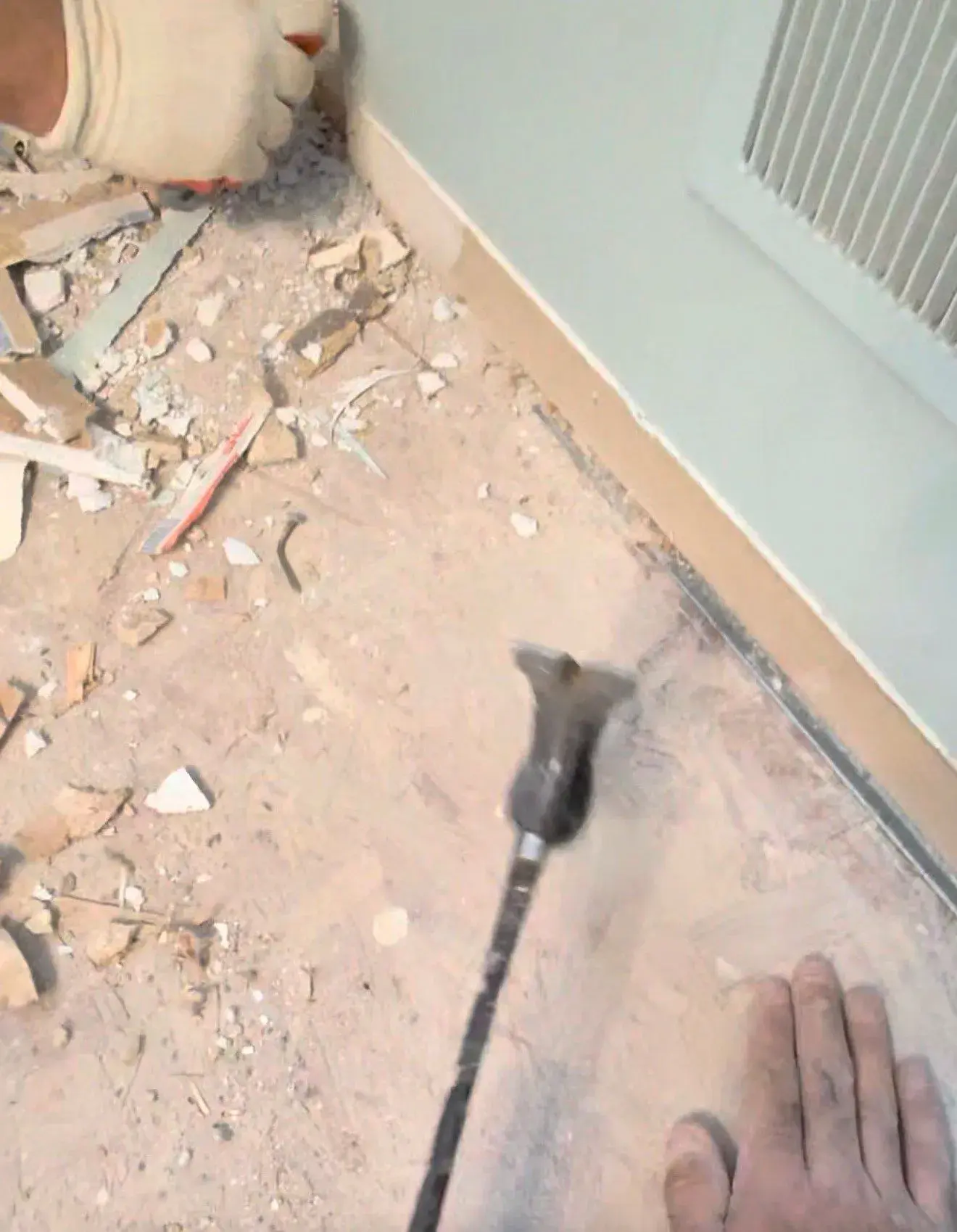 Demolition debris on the exposed bathroom floor as the surface is scraped