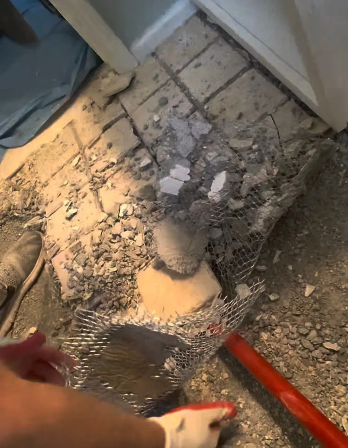Broken tile and mud bed being removed with metal mesh visible in the floor debris